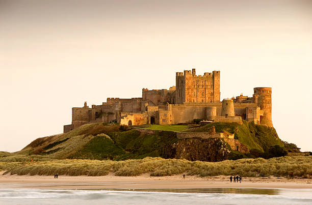 Bamburgh Castle daytime with people walking on beach stock photo