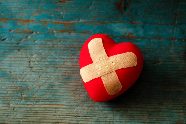 Band-aid covering a heart on a blue wooden background  Emotional Pain stock pictures, royalty-free photos & images