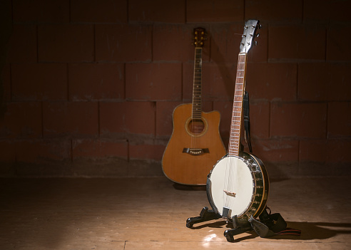 Banjo and a blurry guitar in the background against a dark brick wall in the garage of a music band, copy space, selected focus, narrow depth of field
