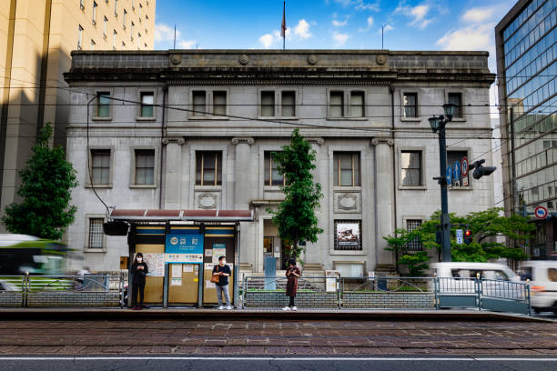 Bank of Japan Bus Stop Hiroshima, Hiroshima Prefecture, Japan - October 9, 2021: People at the trolley stop in front of the Former Bank of Japan Hiroshima Branch, one of the few buildings to survive near ground zero of the atomic bomb blast. BANK OF JAPAN stock pictures, royalty-free photos & images
