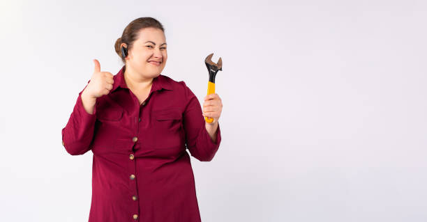 Banner, long format, grey background Female fat mechanic or a plumber, showing thumb up, working hard, holding a wrench, wearing bordo dress and bluetooth headset hardisk format stock pictures, royalty-free photos & images