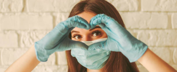 Banner of happy woman looks through hands in form of heart Banner young woman in protective face mask and medical gloves gesturing love shape sign. Happy girl in medical face mask and gloves looking through hands in form of heart symbol. Health care, COVID-19 protection photos stock pictures, royalty-free photos & images