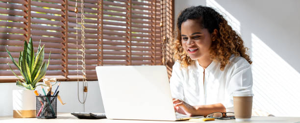 Banner shot of happy young African American business woman working from home on laptop computer in living room stock photo