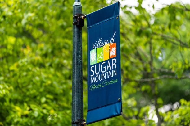 Banner sign closeup at entrance to famous Sugar Mountain ski resort town village in North Carolina on pole post with background of green trees in summer stock photo