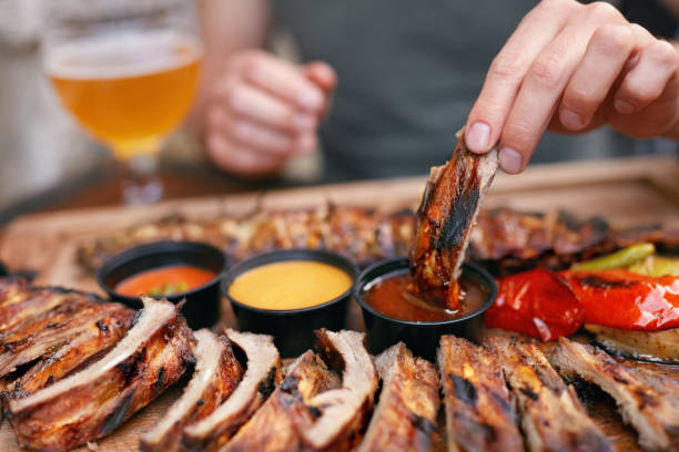 Barbecue Ribs With Sauсes Closeup Barbecue Ribs With Sauсes Closeup. Man's Hand With Spareribs. High Resolution condiment stock pictures, royalty-free photos & images