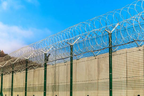 Barbed wire against a blue sky. Prison concept. Entry order. Military base. Detail of New Fence with Barbed Wire Barbed wire against a blue sky. Prison concept. Entry order. Military base. Detail of New Fence with Barbed Wire chain link fence stock pictures, royalty-free photos & images