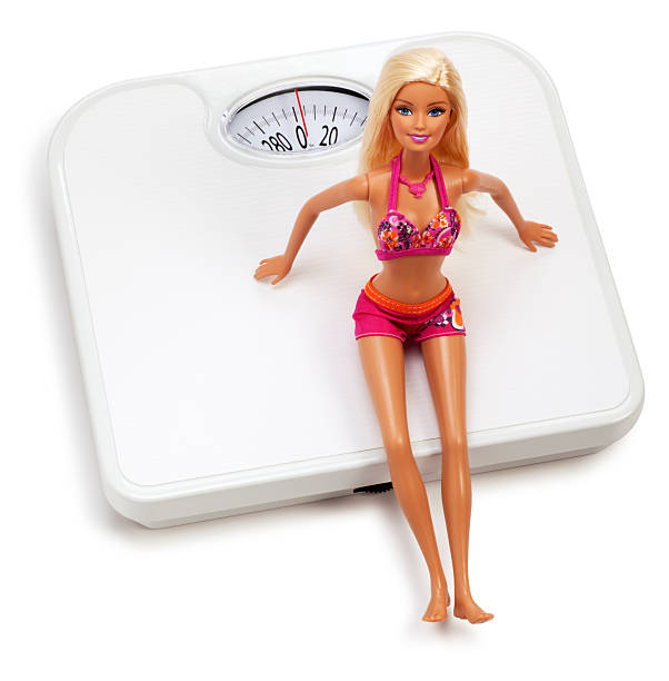 barbie doll sitting on a white scale - barbie stockfoto's en -beelden