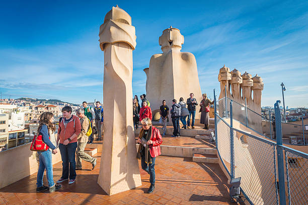 Barcelona tourists beside iconic Gaudi chimneys on La Pedrera Spain Barcelona, Spain - 14th February 2013: Tourists enjoying their visit to the rooftop of Casa Mila, La Pedrera, to see the iconic Gaudi chimneys that overlook the Sagrada Familia and the heart of downtown Barcelona, Spain. casa milà stock pictures, royalty-free photos & images