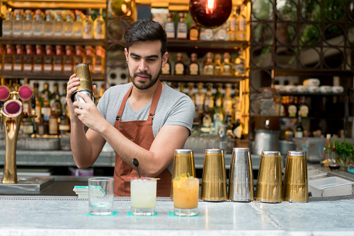 Happy Latin American male bartender making cocktails at a bar