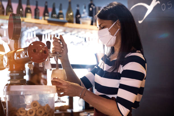 Bartender serves a fresh beer in a pub Bartender serves a fresh beer in a pub in the pandemic days, wearing protective face mask. small business saturday stock pictures, royalty-free photos & images