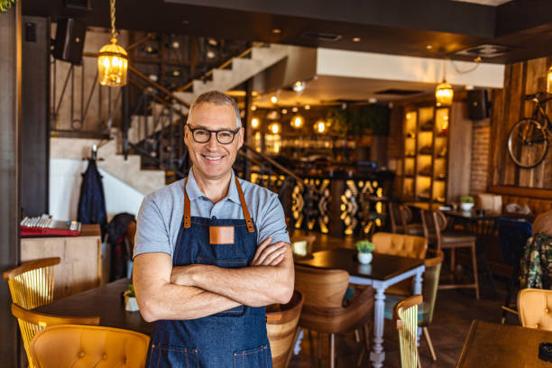 Bartender wearing apron and smiling Proud, mature café owner with apron standing on the door of restaurant and looking at camera, smiling Restaurant stock pictures, royalty-free photos & images