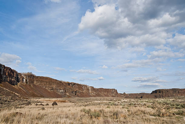 Basalt Cliffs and Grassland in Ancient Lakes Basin East of the Cascade Mountains, Washington’s climate is arid and the terrain is desert-like. Summertime temperatures can exceed 100 degrees Fahrenheit in regions such as the Yakima Valley and the Columbia River Plateau. This is an area of rolling hills and flatlands. During the last Ice Age, 18,000 to 13,000 years ago, floods flowed across this land, causing massive erosion and leaving carved basalt canyons, waterfalls and coulees known as the Channeled Scablands. The Quincy Lakes area is part of the scablands of central Washington State. Visitors to this area will experience basalt cliffs, mesas, benches, canyons and potholes. Several of the potholes have become lakes that are filled with water seeping from the irrigation of nearby upslope farmlands. Ancient and Dusty lakes are two examples that have added to fish and wildlife diversity and have also become important recreational areas. Ancient Lake and Dusty Lake are in the Quincy Wildlife Recreation Area near Quincy, Washington State, USA. jeff goulden washington state desert stock pictures, royalty-free photos & images
