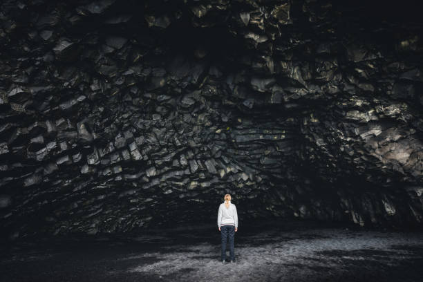 Basalt Columned Wall In Iceland Woman standing in the basalt cave Halsanefshellir on the famous black-sand beach Reynisfjara. basalt stock pictures, royalty-free photos & images