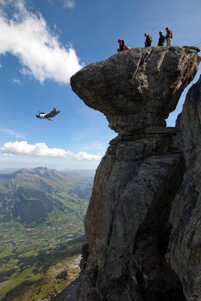 Base jumper/ wingsuiter launches off cliff in the Alps Lofty skies above and below base jumping stock pictures, royalty-free photos & images