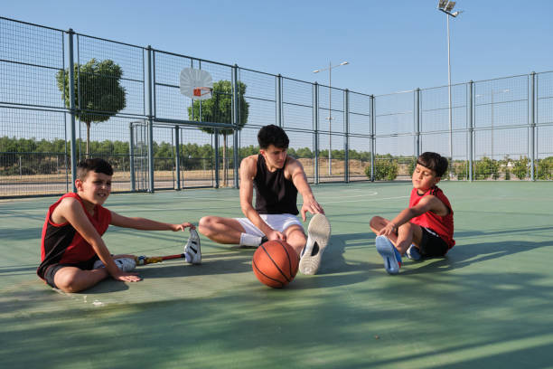Basketball coach doing leg stretching exercises with two children. stock photo