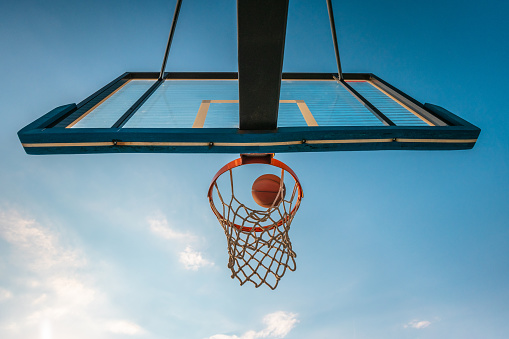 Shot from below at the basketball hoop, bank shot, ball flying towards the back board and hoop on a clear day