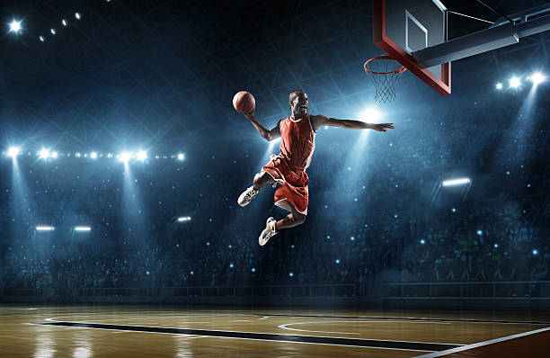 Basketball player makes slam dunk Close up image of professional basketball player about to do slam dunk during basketball game in floodlight basketball court basketball stock pictures, royalty-free photos & images