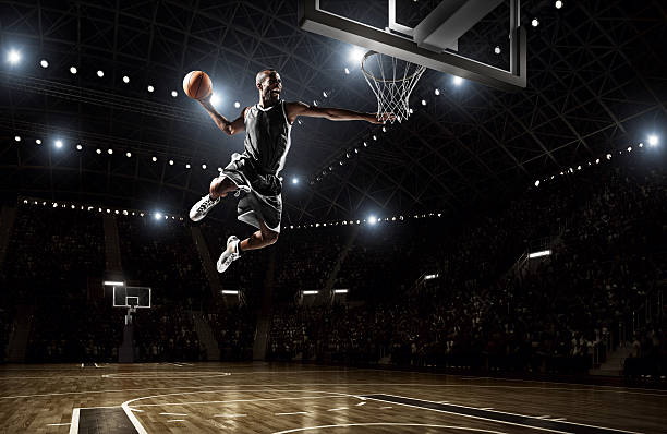 Basketball player makes slam dunk Close up image of professional basketball player about to do slam dunk during basketball game in floodlight basketball court tall high stock pictures, royalty-free photos & images