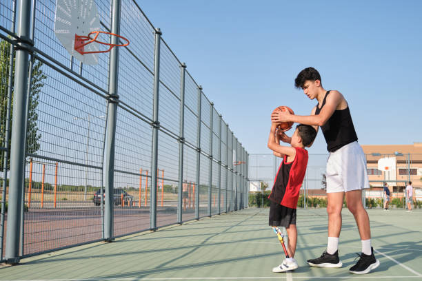 Basketball trainer showing how to shoot basketball to a child with a leg prosthesis. Coach training a kid. stock photo