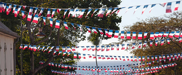 Panoramic view of garlands of french flags hanging form one side to another side of a street with the sky and ocean on the background. Those decorations are to celebrate Bastille Day (