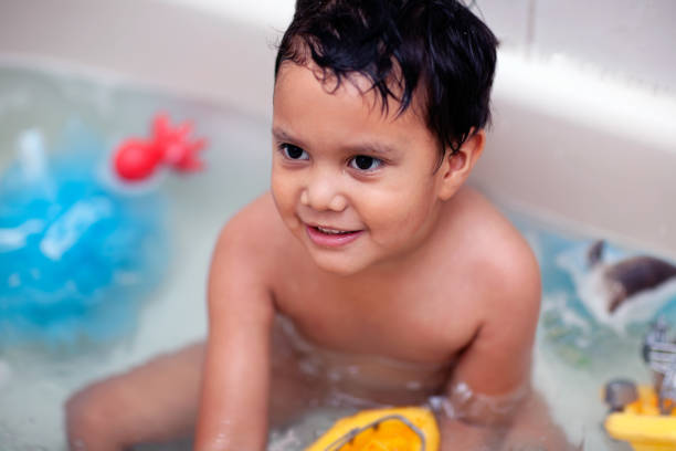 Bath time with a boy sitting in the tub and playing with toddler water toys. stock photo