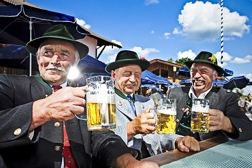 Three Bavarians in Traditional Clothing Drinking Beer and Celebrating in a Beergarden.
