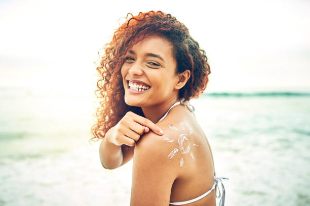 Be like me, apply sunscreen Cropped portrait of an attractive young woman pointing at sunscreen on her back at the beach sunscreen stock pictures, royalty-free photos & images