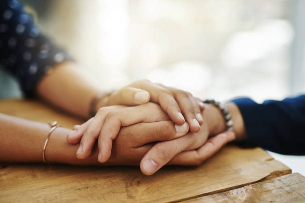 Be the person who helps the next Closeup shot of two unrecognizable people holding hands in comfort mourner stock pictures, royalty-free photos & images