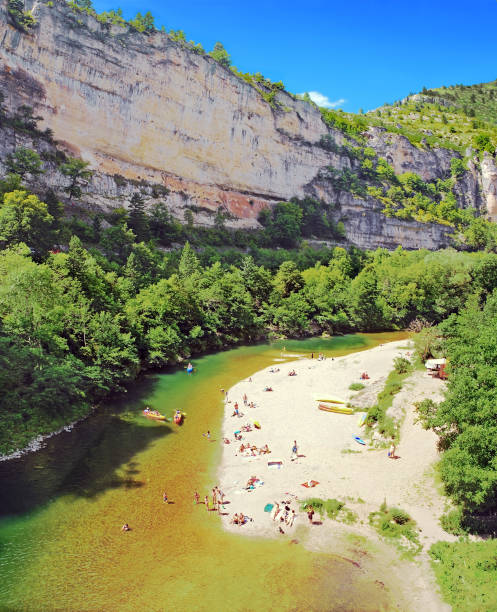 Beach and cliff of Tarn. Occitanie. France. Saint-Chely Tarn. July 31, 2014. The river flows at the foot of the cliffs of the canyon. The pebble beaches are occupied by holidaymakers who like to swim or canoe. gorges du tarn stock pictures, royalty-free photos & images