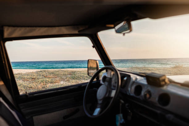 beach at sunset viewed from inside old car window. - front view old jeep stockfoto's en -beelden