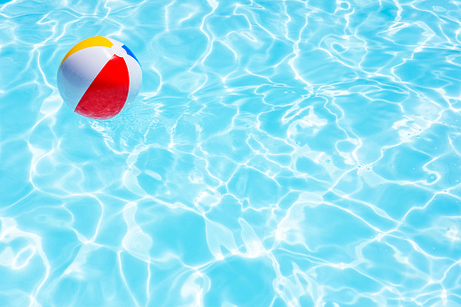 Beach ball floating in swimming pool background concept for summer vacation, relaxation and fun in the sunshine