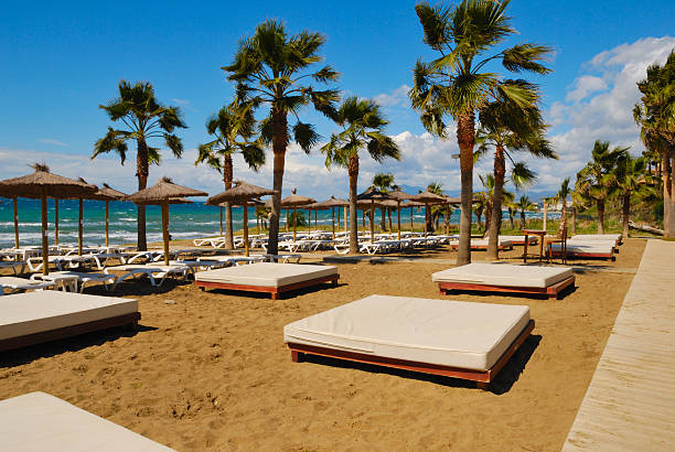 Beach resort located in Marbella (Spain) Lonely sunbeds and umbrellas beach in a windy day in beach resort located in Marbella (Spain) marbella stock pictures, royalty-free photos & images