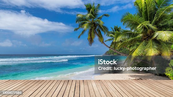 istock Beach wooden table and coconut palms with party on tropical beach background. 1300077585