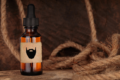 Beard oil, barbershop product photography. Brown bottle, mock-up. Bottle with extract on wooden background.