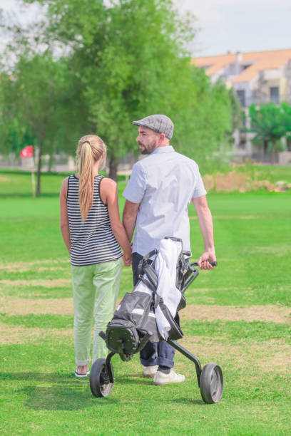 A bearded man looks back as he carries a wheelbarrow across a golf...