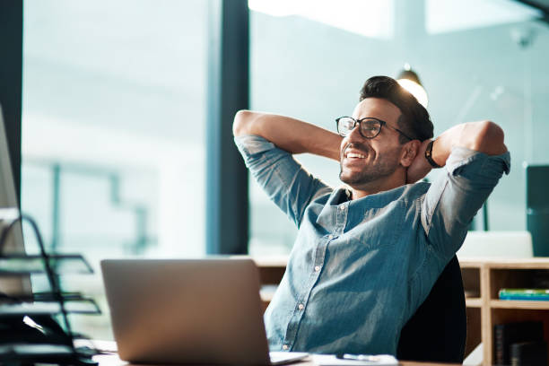 Beating the deadline like the champ he is Shot of a young businessman taking a break at his desk in a modern office carefree stock pictures, royalty-free photos & images