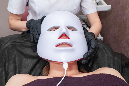 Beautician puts mask on patient face for light treatment procedure