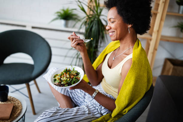 schöne afro amerikanische frau essen gemüsesalat zu hause. - woman happy eat stock-fotos und bilder