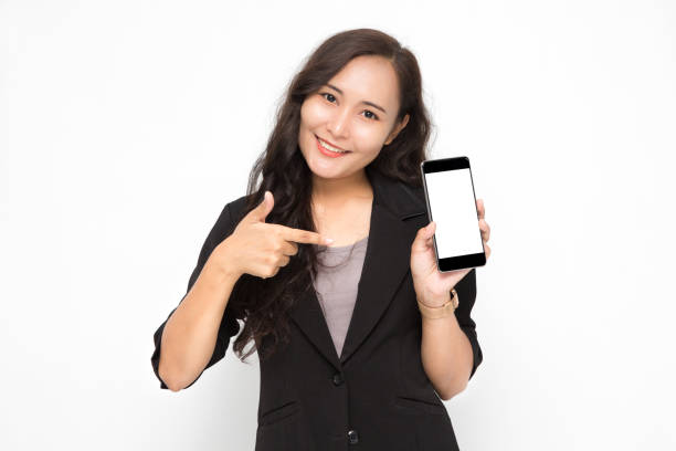 Beautiful Asian business woman wearing black suit hand holding a smartphone and pointing presenting something on white background and copy space.  Confident Asian working woman smiling and cheerful stock photo