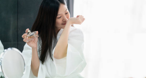 mulher asiática bonita no vestido de banho branco apreciar o bom cheiro do fundo novo do banheiro do perfume - perfume - fotografias e filmes do acervo