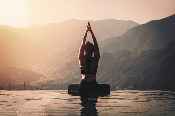美麗迷人的亞洲婦女練習瑜伽蓮花姿勢在游泳池上方的山峰上的早晨在美麗的自然景觀前, 感覺如此舒適和放鬆在假期, 溫暖的色調 - yoga 個照片及圖片檔