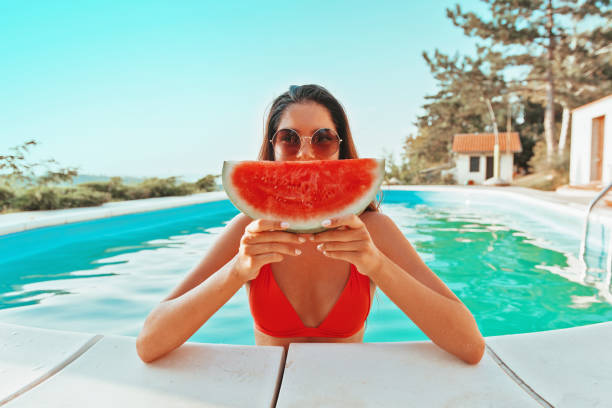 bella donna attraente che si gode in piscina, tenendo in mano un anguria - frutta estate foto e immagini stock