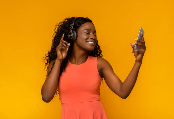 Beautiful black girl enjoying music with wireless headset Beautiful african girl enjoying music with wireless headset, holding smartphone with closed eyes, yellow background headphones photos stock pictures, royalty-free photos & images
