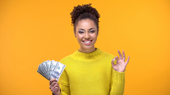 Beautiful black lady showing bunch of dollars and ok gesture, cash-back service