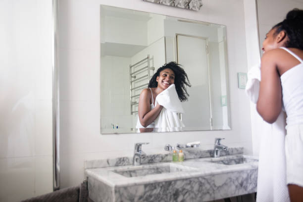 Beautiful black woman drying her face with a towel while looking at herself in the mirror smiling Beautiful black woman drying her face with a towel  in the bathroom while looking at herself in the mirror smiling drying stock pictures, royalty-free photos & images