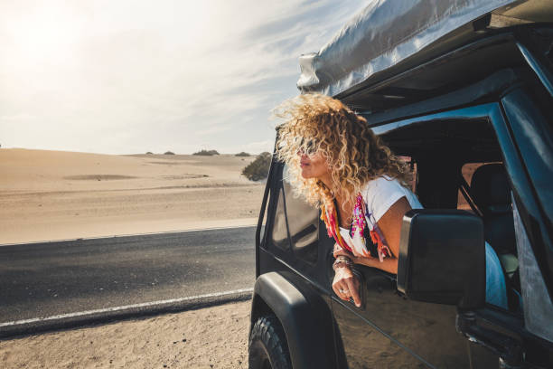 beautiful blonde curly hair adult young woman outside the car enjoying the travel lifestyle and alternatie vacation with tent on the roof and free camping everywhere - people traveling - desert backgorund - cargo canarias imagens e fotografias de stock