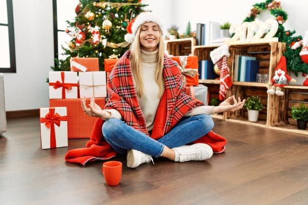 Beautiful blonde woman sitting on the floor by christmas tree relax and smiling with eyes closed doing meditation gesture with fingers. yoga concept. stock photo