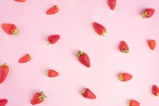 Beautiful colorful pattern made of fresh hand-arranged strawberries on a bright pink background. Flat lay creative design.