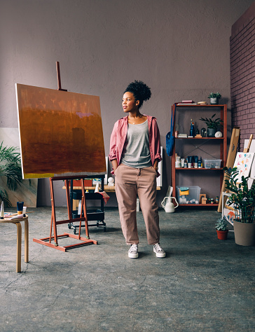 A creative female painter dressed in a pink shirt, standing in her home studio.