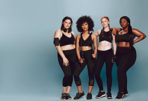 Beautiful curvy women with good body Full length of multi-ethnic women with  in sportswear standing together over grey background. Three women of different race, figure type and size in fitness clothing. body positive stock pictures, royalty-free photos & images
